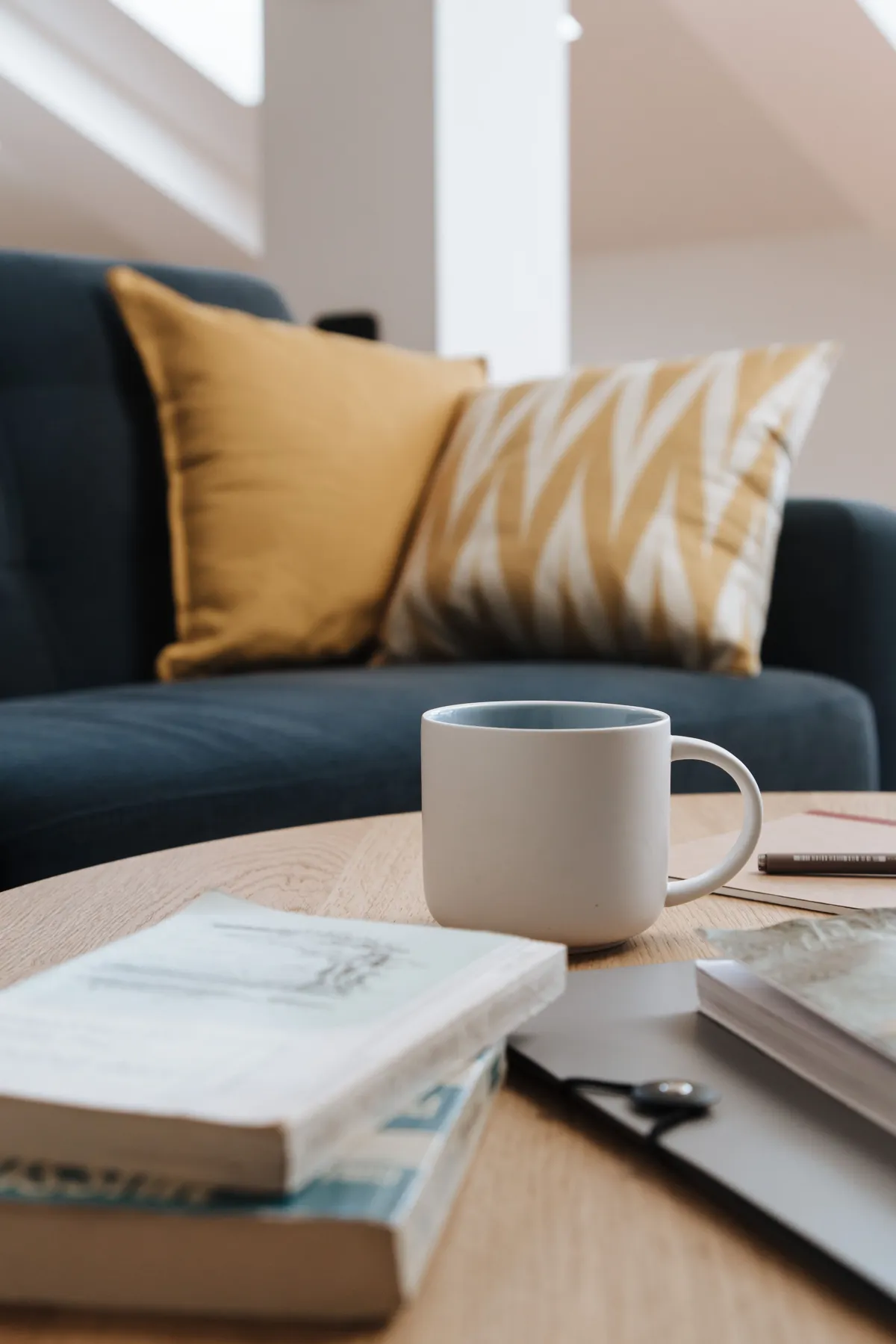 A mug and books on a coffee table in front of a sofa with cushions