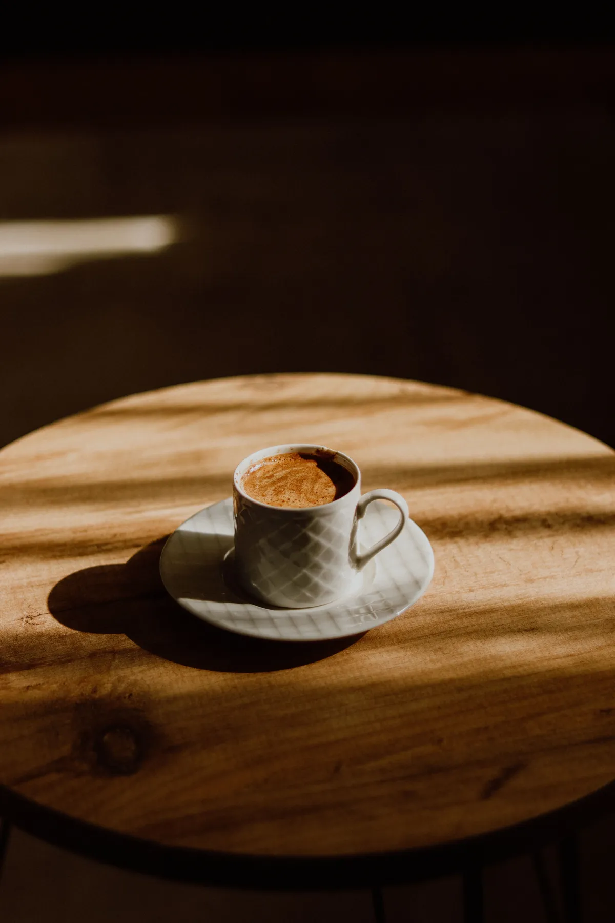 A cup of coffee on a round wooden table in warm afternoon light